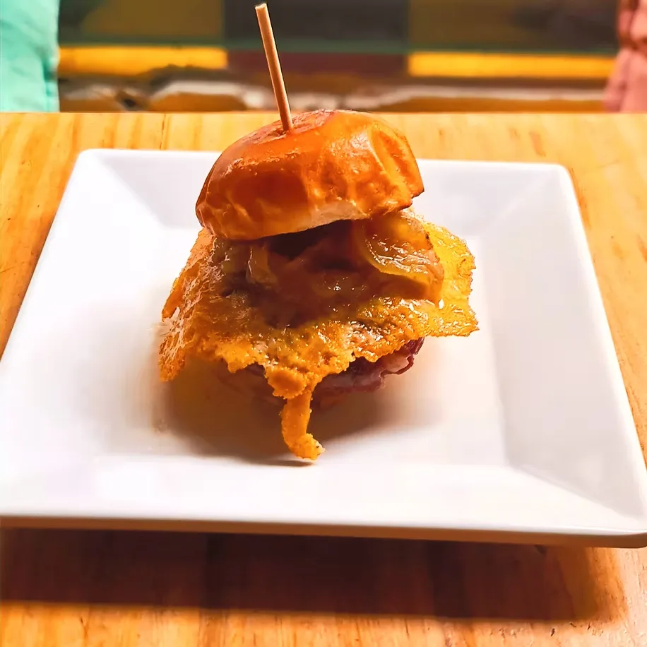Mini burger de ternera con queso fundido y cebolla caramelizada, servida en plato blanco